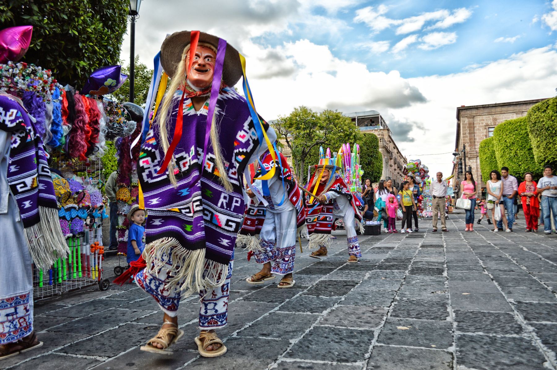 Danza tradicional con máscaras y trajes bordados en una calle de México